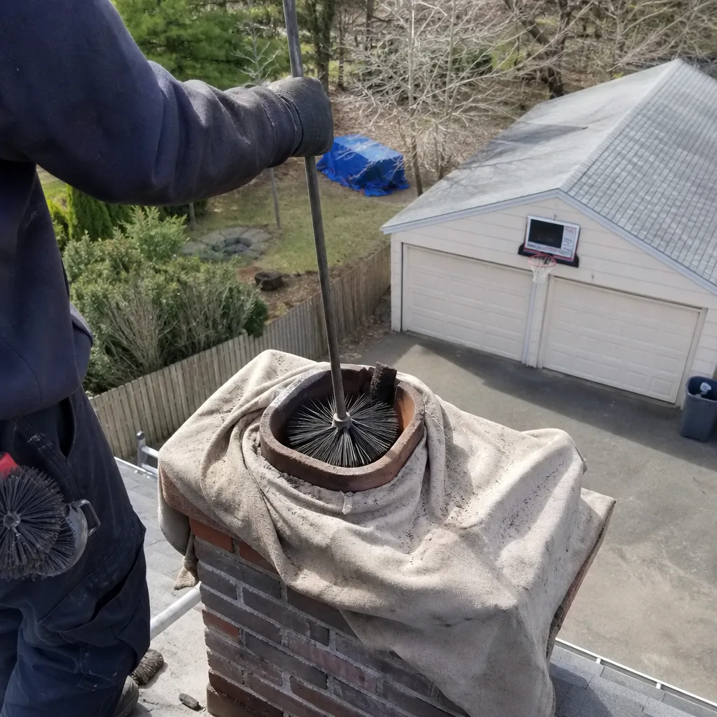 Professional chimney sweep cleaning a brick chimney flue from the roof