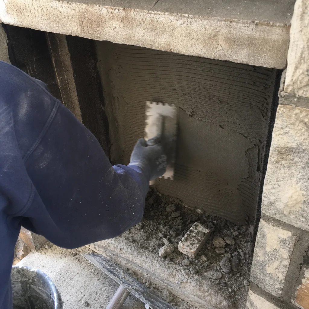 Professional applying mortar to a fireplace wall with a notched trowel